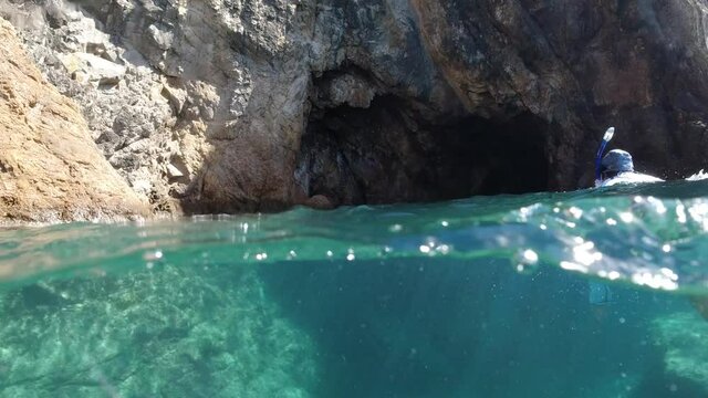 snorkeler swimming toward a sea cave.  Unique below and above water bubble camera view in the British Virgin Islands