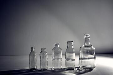 A five different empty glasses bottles with copy space. Graphic still life with light and shadow in gray light. The concept of containers, recyclable materials or alcoholism. Creative vintage vase