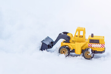 Yellow excavator removes snow on the road.