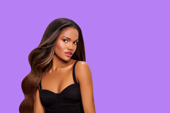 Beauty styled Portrait of a young African-American Woman with long curly hair in black Dress. Makeup. Fashion black woman with Curly Hair posing in the Studio on a light purple background. isolated. 