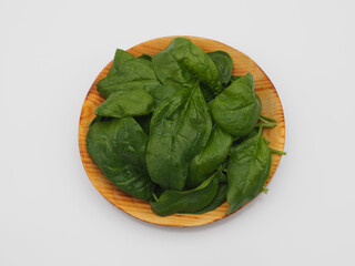 Isolated fresh green spinach leaves in a wooden plate on a white background. Useful spicy herb spinacia for dietary nutrition, closeup.Eco-friendly gardening, horticulture and crop production