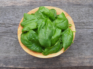 Fresh green spinach leaves in a wooden plate on a wooden table. Useful spicy herb spinacia for...