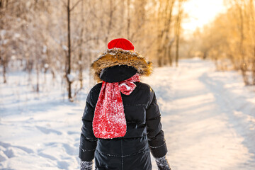 Cute little girl 10 years old in a red hat in a winter forest with sunlight. A little girl is having fun on a winter day. cheerful little girl in a warm jumpsuit