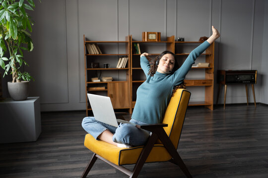 Happy office-based female employee trying to adapt to remote work from home during Covid-19, young relaxed woman freelancer in headset stretching arms with closed eyes, taking break from computer