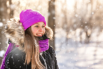 Portrait of a charming little girl in a purple hat in a snowy forest in winter. Christmas winter holidays. Happy childhood