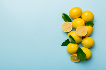 Many fresh ripe lemons with green leaves on colored background, top view, space for text