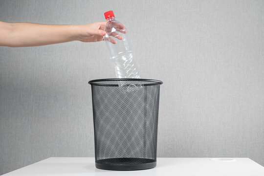 hand of an unrecognizable woman throws a plastic bottle into the trash can.