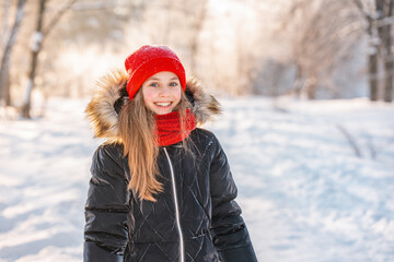 Fototapeta na wymiar Portrait of a charming little girl in a red hat in a snowy forest in winter. Christmas winter holidays. Happy childhood