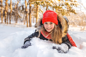 A happy little girl with pink cheeks lies on a snowdrift and laughs in a beautiful winter forest