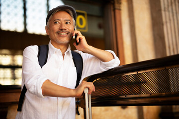 Happy senior man waiting a train. Man talking to the phone while waiting a train. Man preparing for the trip.