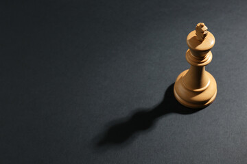 White wooden chess king on dark background, above view. Space for text