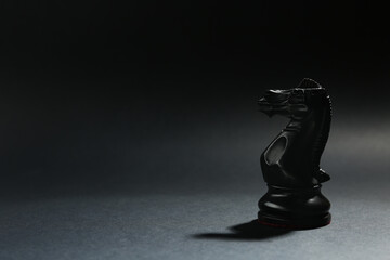 Black wooden chess knight on dark background. Space for text