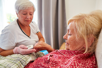 Altenpflegerin misst Herzfrequenz bei kranker Seniorin