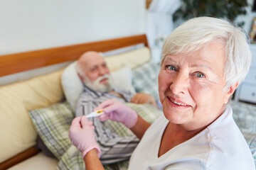 Pflegedienst mit Fieberthermometer am Bett von krankem Senior
