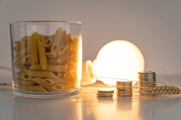 Ear of wheat, pasta, light bulb and coins, on white surface. Price of energy and wheat, which...