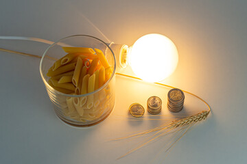 Ear of wheat, pasta, light bulb and coins, on white surface. Price of energy and wheat, which...