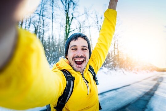 Young man wearing winter clothes taking selfie picture in winter snow forest - Happy guy with backpack hiking outside - Recreation, sport and people concept