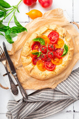 Fresh homemade galette with tomatoes, ricotta cheese and basil on white tile background. Top view.