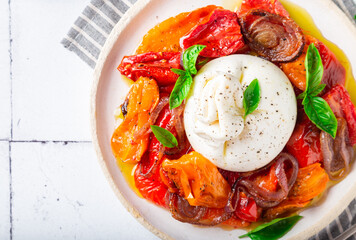 BurBurrata cheese with baked tomatoes, pepper, red onion and fresh basil on white tile background. Traditional italian food. Top view. Close-up.