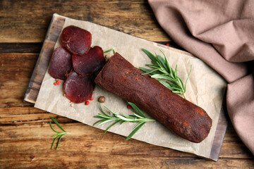 Delicious dry-cured beef basturma with rosemary and peppercorns on wooden table, flat lay