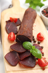 Delicious dry-cured beef basturma with basil and tomatoes on table, closeup