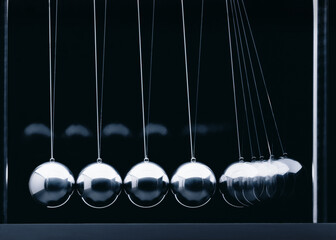 Newton-Pendel mit 5 silbernen Kugeln hintereinander, seitlich fotografiert vor Hintergrund in dunkelgrau
