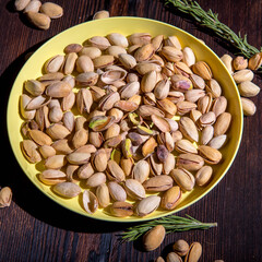Pistachio nuts in a yellow bowl on a wooden background, side view, copy space