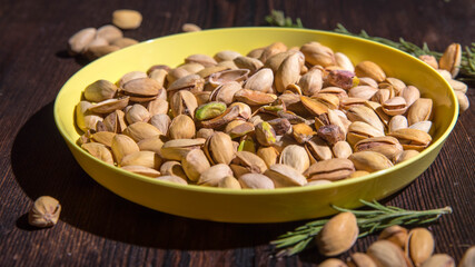 Pistachio nuts in a yellow bowl on a wooden background, side view, copy space
