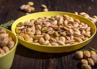 Pistachio nuts in a yellow bowl on a wooden background, side view, copy space