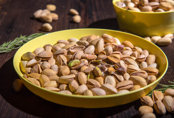 Pistachio nuts in a yellow bowl on a wooden background, side view, copy space