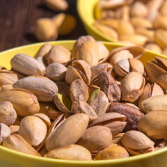 Pistachio nuts in a yellow bowl on a wooden background, side view, copy space