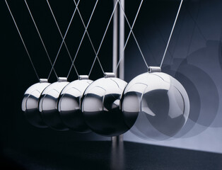 Newton-Pendel mit 5 silbernen Kugeln aus Metall in Bewegung, hintereinander, vor Hintergrund in dunkelblau