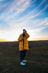 Traveler man in yellow coat with smartphone walking on hill looking at sunset sky . Authentic male tourist with gadget lifestyle. Hipster guy outdoor Solo travel adventure. Active walking backpacking.