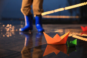 Little boy outdoors, focus on paper boats in puddle