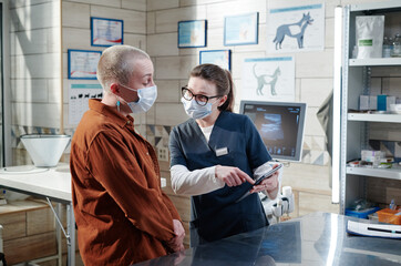 Vet doctor in uniform pointing at digital tablet and explaining something to the client in vet...