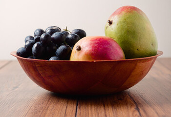 Naklejka na ściany i meble Fresh mango and dark grapes in a small wooden bowl and table. Still life. Light and rich saturated color.
