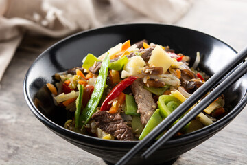 Beef, vegetables and sesame seeds in black bowl on wooden table. Close up	