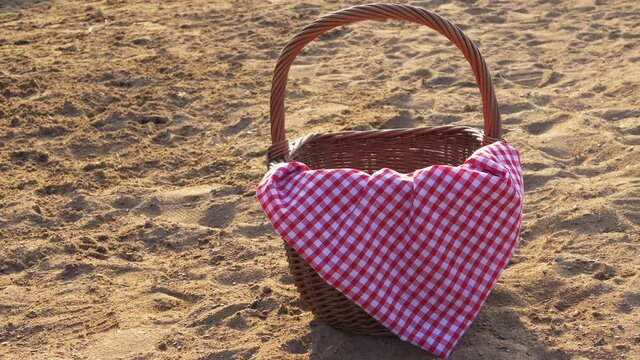 Picnic basket with red gingham cloth on the beach sand 