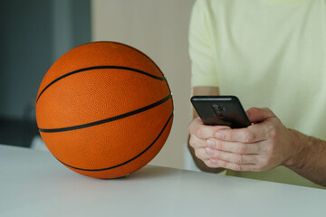 Close up of young man with basketball ball betting in internet with the smartphone.