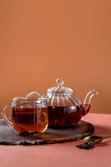 Glass teapot, cup of tea and tea leaves on brown background. Hot herbal tea is in the glass teapot on the table. Copy space.