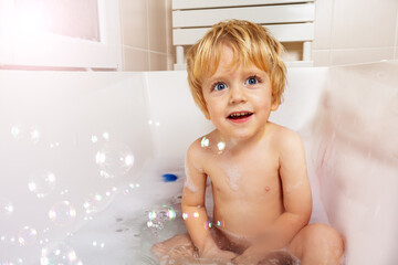 Happy baby boy play with soap bubble in bathroom