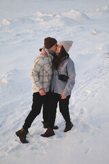 Guy in fashionable clothes kisses a girl on the cheek in winter on a walk on a snowy lake