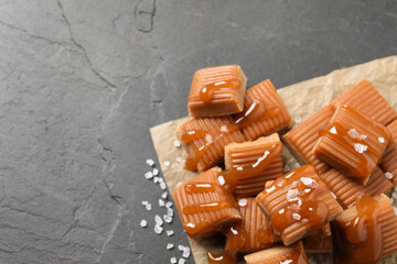 Tasty caramel candies with sauce and sea salt on grey table, above view. Space for text