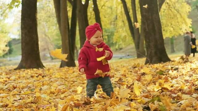 Laughing child standing in autumn park with falling leaves. Happy moment of mother playing with child. Carefree childhood. Family concept