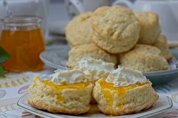 Close up of fresh scones topped with homemade apricot jam and whipped cream with jam jar and scones...