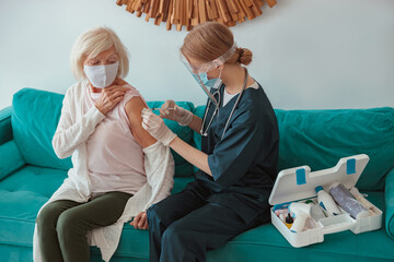 Nurse giving injection to senior woman in living room