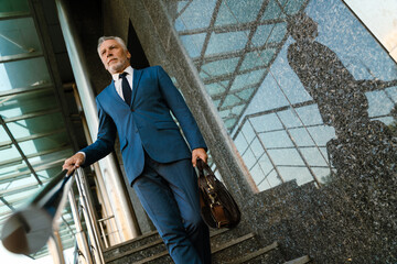 Senior grey man dressed in suit going down stairs