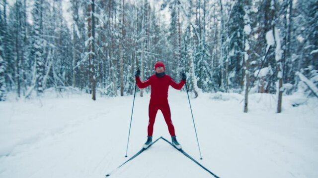 Ski in the forest, dolly in. Young man in red suit stands in the winter forest and looks into the camera.