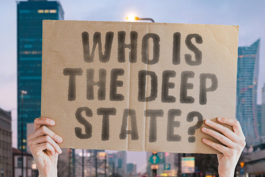 The question " Who is the deep state? " on a banner in men's hand with blurred background. Administration. Rule. Care. Agreement. Union. Manipulation. Pressure. Exploitation