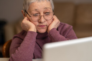 A senior woman sitting in front of a laptop communicates online through social networks.